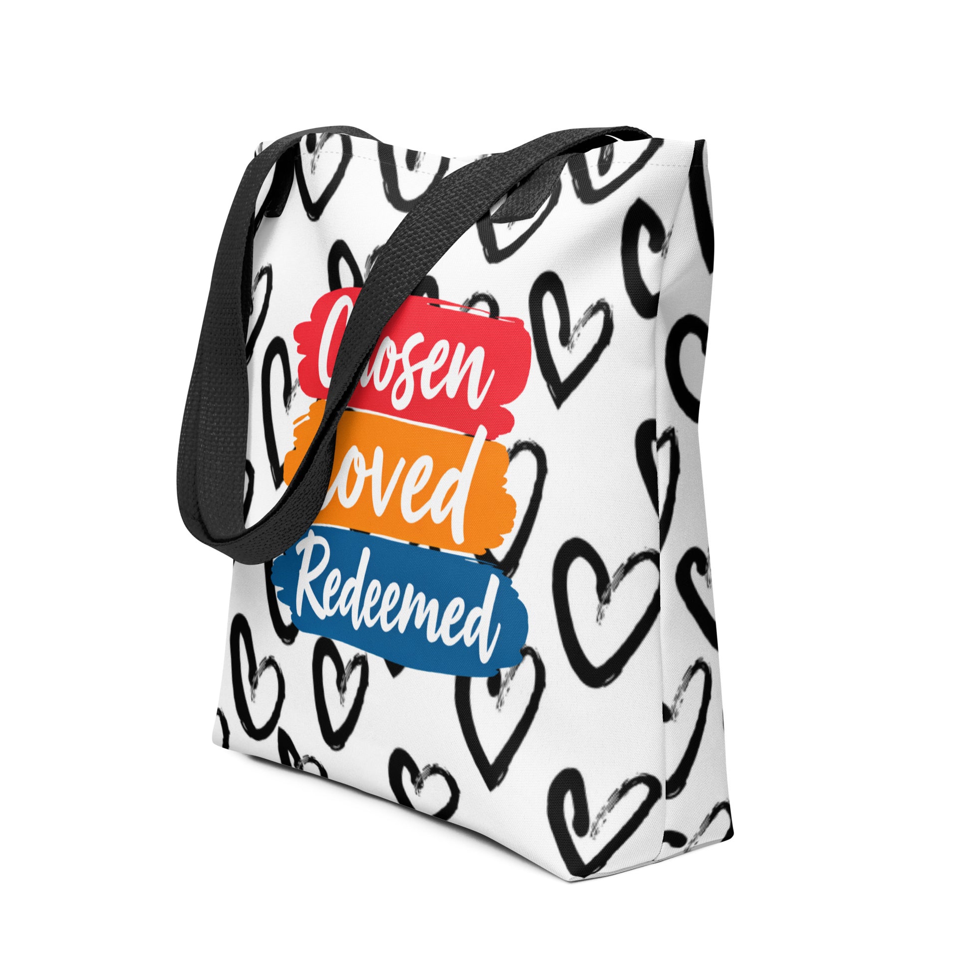 Angled view of the white tote with black straps showing the black heart print and "Chosen Loved Redeemed" brushstroke design.