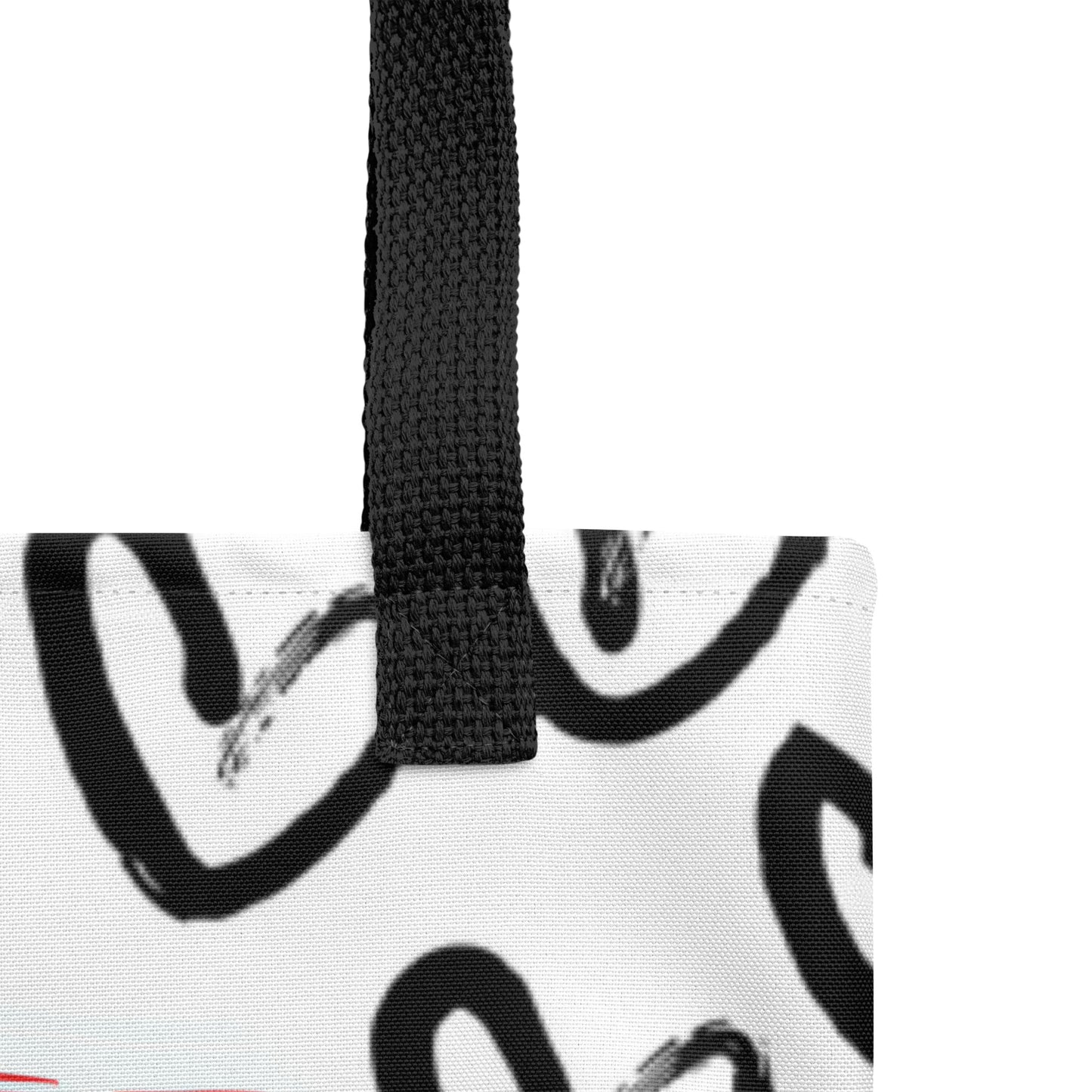 Close-up of the white tote fabric and black strap, highlighting the stitching, textured canvas, and black heart-and-brush pattern detail.