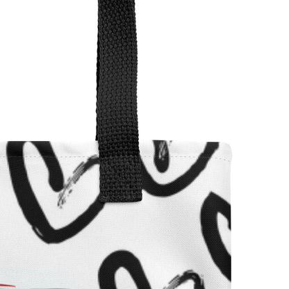 Close-up of the white tote fabric and black strap, highlighting the stitching, textured canvas, and black heart-and-brush pattern detail.