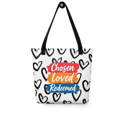 Tote bag hanging on a hook with black handles, featuring an all-over black heart pattern and "Chosen Loved Redeemed" graphic.