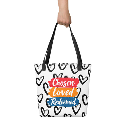 Tote bag held in hand with black handles, black heart print, and the "Chosen Loved Redeemed" stacked brushstroke design.