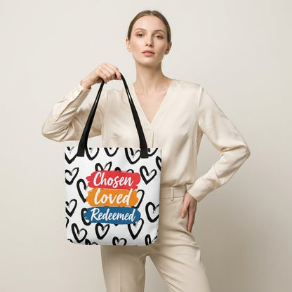 Model carrying a white tote with black handles featuring the black heart pattern and “Chosen Loved Redeemed” design.