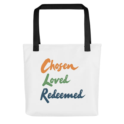 Front view of a white tote bag with black handles featuring the words “Chosen Loved Redeemed” in orange, green, and navy script.
