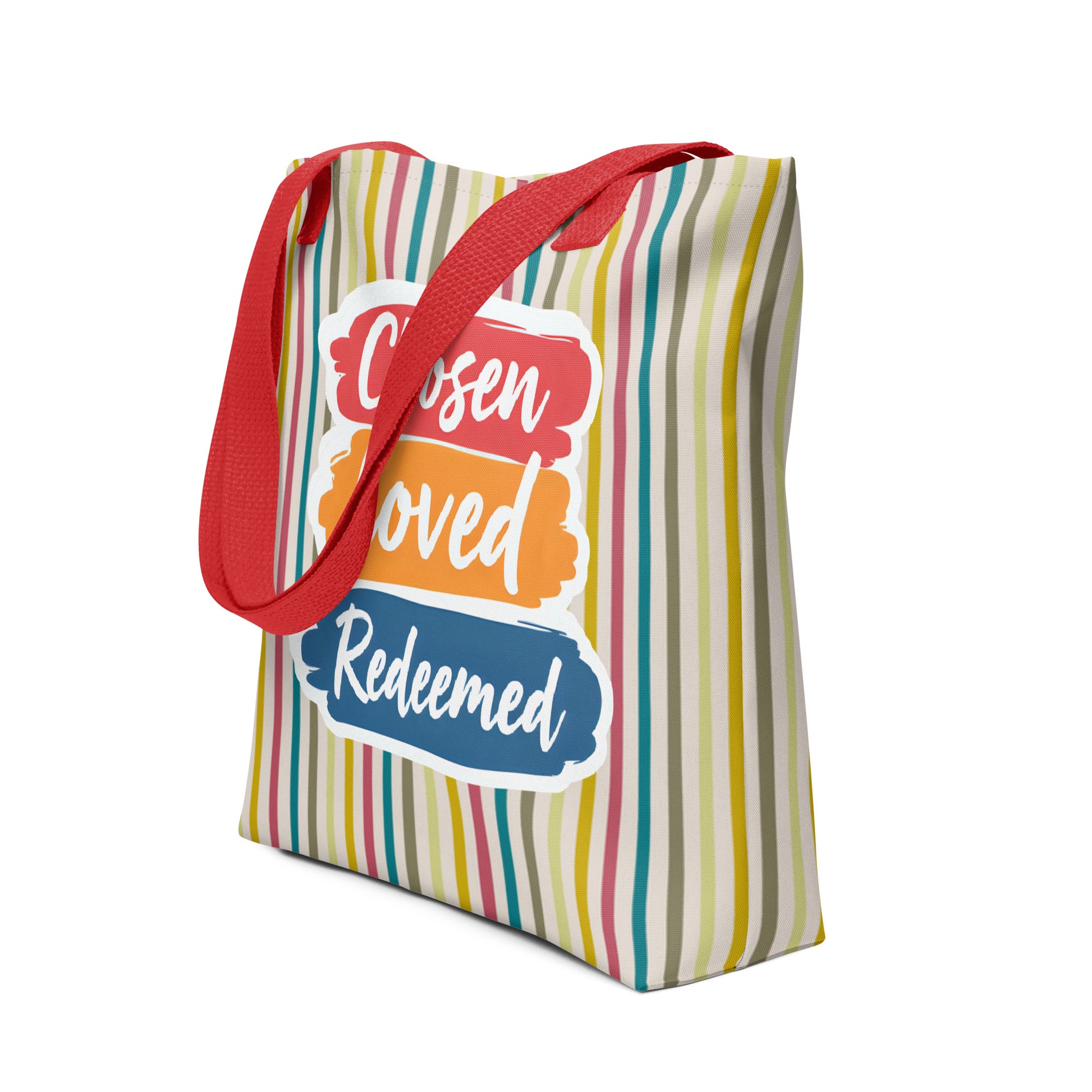 Angled view of a multicolor striped tote with red straps showing “Chosen Loved Redeemed” in white script on stacked brushstroke panels.