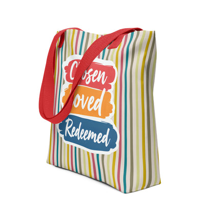 Angled view of a multicolor striped tote with red straps showing “Chosen Loved Redeemed” in white script on stacked brushstroke panels.