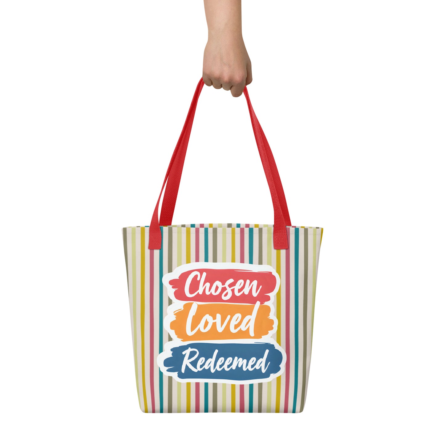 Striped tote bag held in hand with red straps featuring “Chosen Loved Redeemed” in white script on colorful brushstroke blocks.