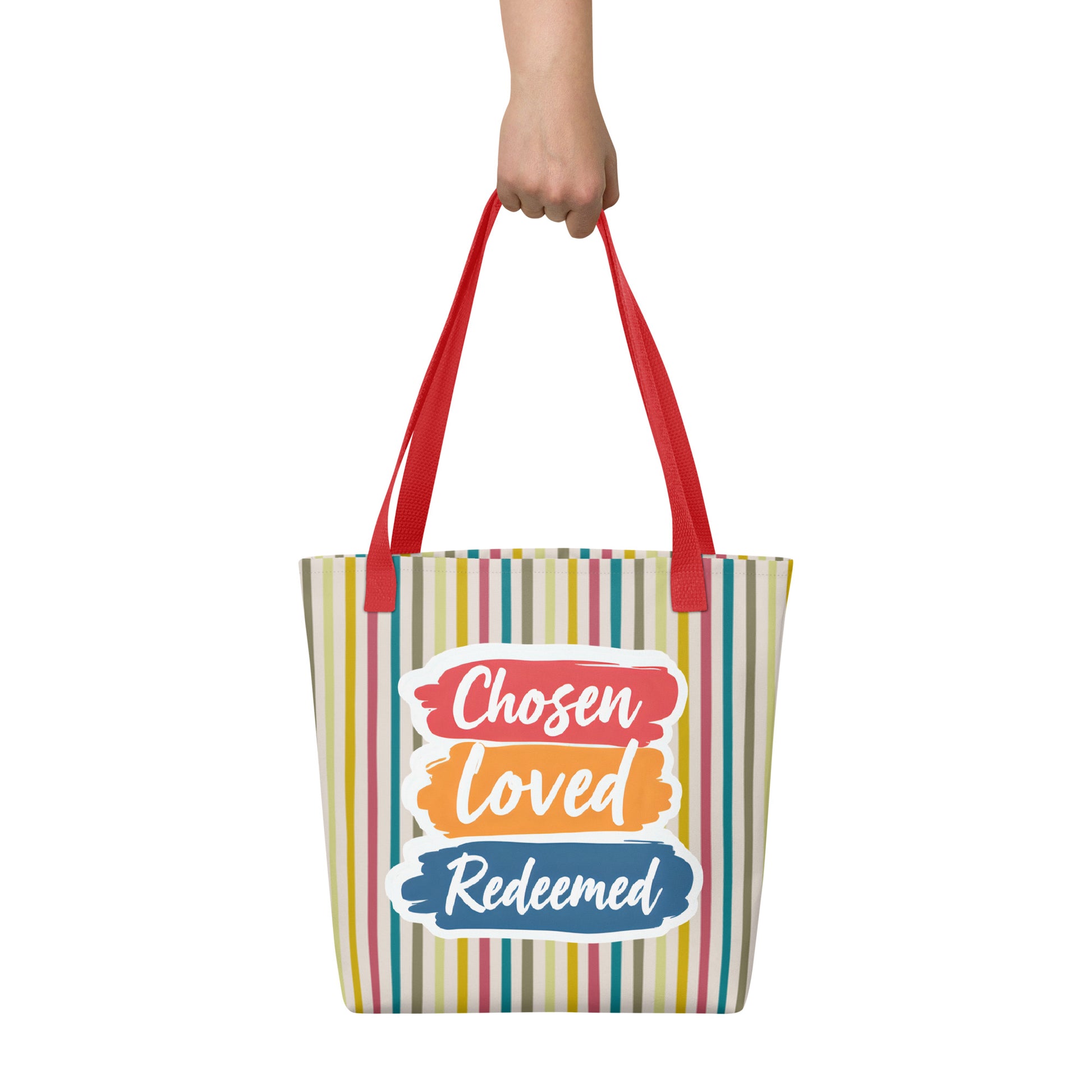 Striped tote bag held in hand with red straps featuring “Chosen Loved Redeemed” in white script on colorful brushstroke blocks.