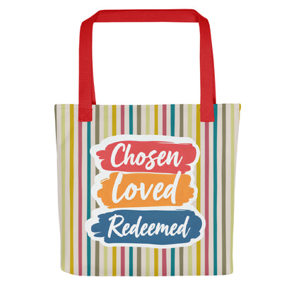 Front view of a striped tote bag with red handles featuring “Chosen Loved Redeemed” in white script on red, orange, and blue brushstroke blocks.