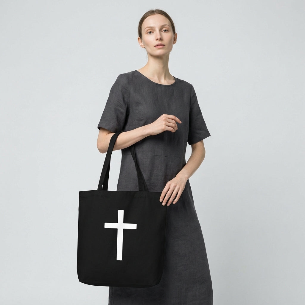 Model holding a black cotton tote bag featuring a large white cross design on the front.