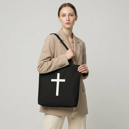 Model holding a black cotton tote bag featuring a large white cross design on the front.