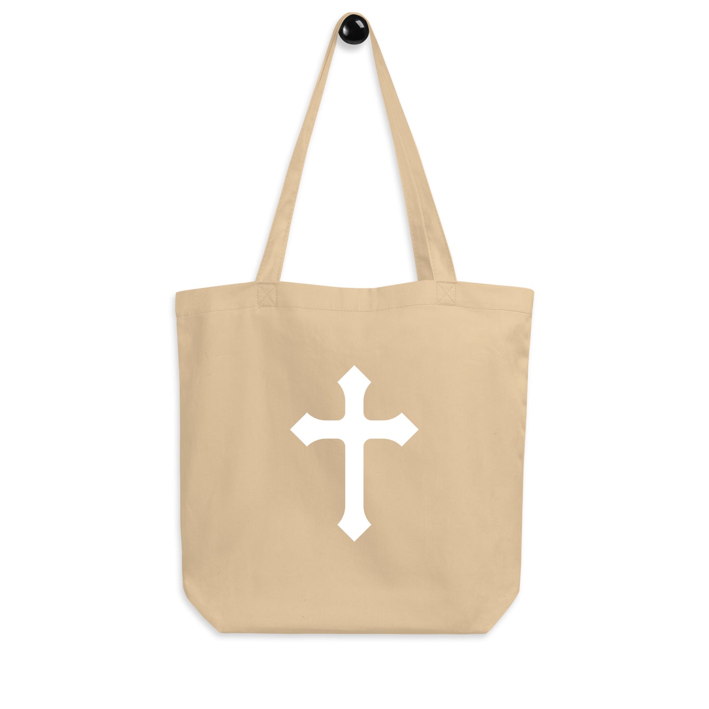 Natural cotton tote bag hanging on a hook, featuring a centered white cross design.