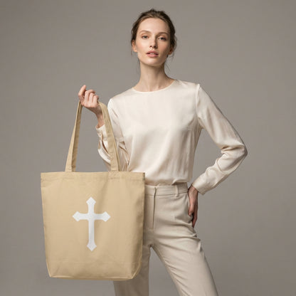 Model holding a natural cotton tote bag with a large white cross graphic on the front.