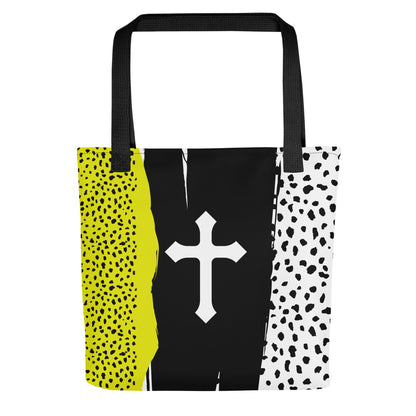 Front view of a bold color-block tote bag with black straps, featuring a white cross on a black brushstroke panel with neon yellow and white speckled side sections.