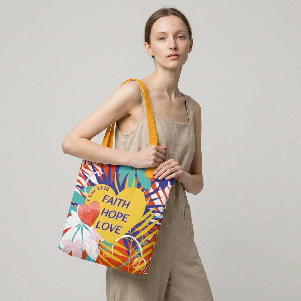 Lifestyle photo of a model holding a colorful floral tote bag with mustard-yellow handles featuring “Faith Hope Love” and “1 Corinthians 13:13.”
