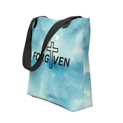 Angled view of the blue watercolor tote featuring “FORGIVEN” across the center with a cross graphic, finished with black handles.