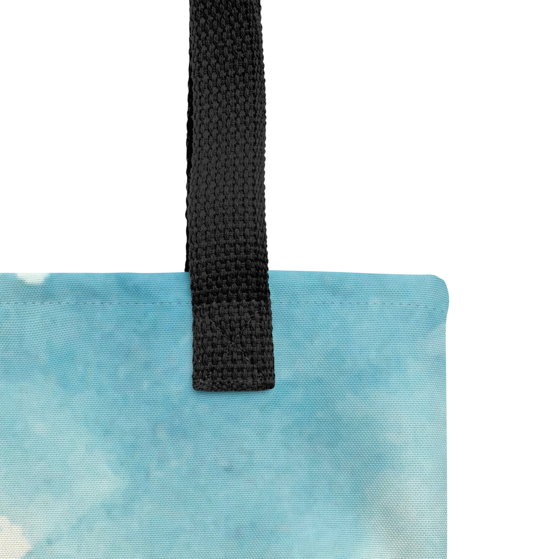 Close-up of the tote’s black woven strap and top seam on a light blue watercolor-printed fabric, showing the canvas texture and stitching.
