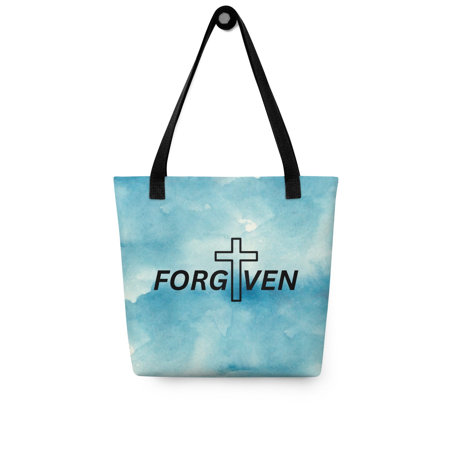 Blue watercolor “FORGIVEN” tote bag with black straps hanging on a hook, showing the centered cross-and-text design.