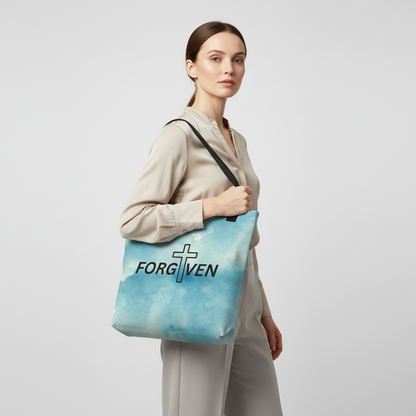 Model wearing a blue watercolor “FORGIVEN” tote with black straps, featuring a cross-and-text Christian design.