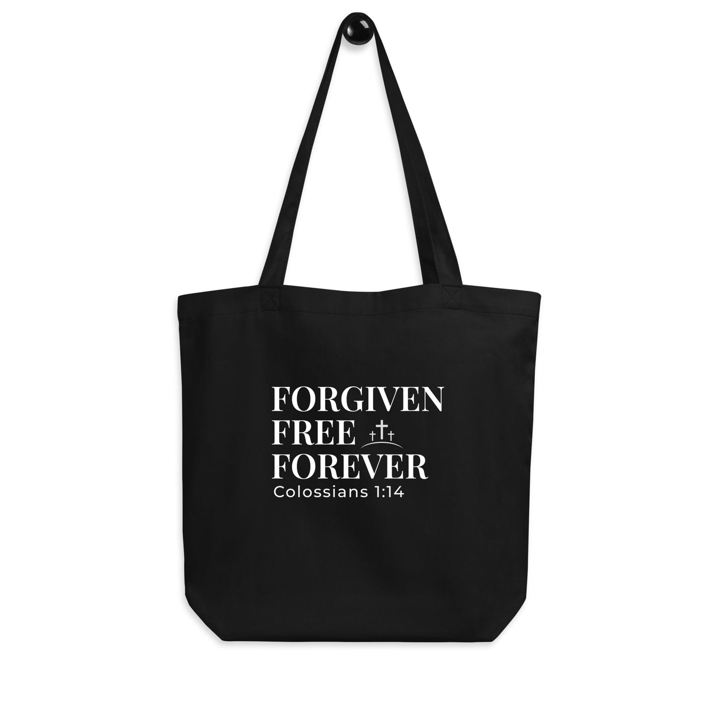 Black tote bag hanging on a hook with “Forgiven Free Forever” and “Colossians 1:14” printed in white with a cross symbol.