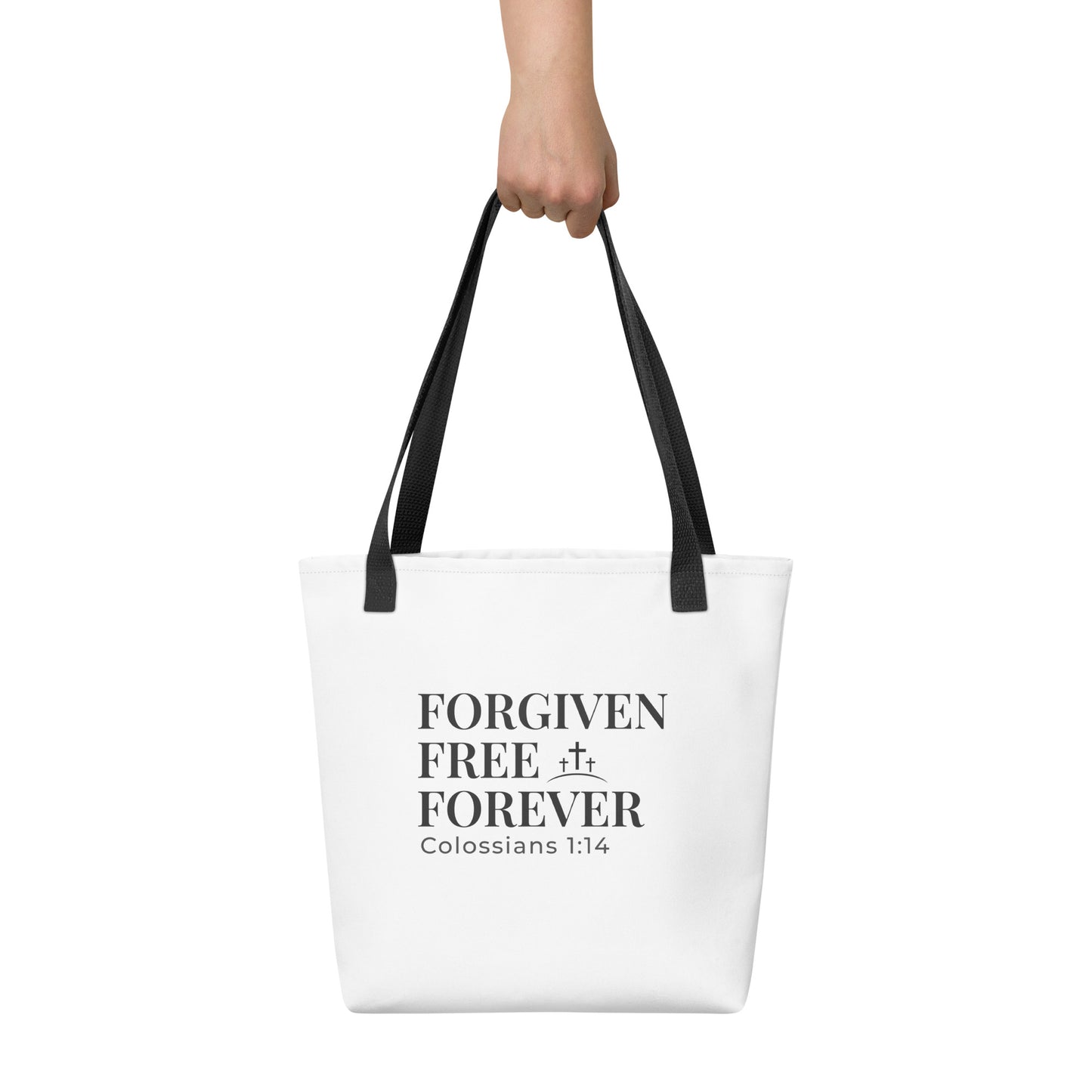 White tote bag held in hand featuring the phrase “Forgiven Free Forever” in bold black lettering and a cross symbol.