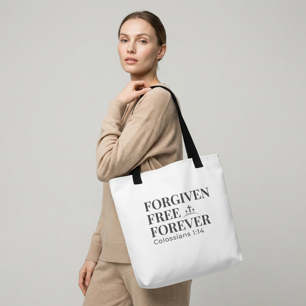 Model holding a white tote bag printed with “Forgiven Free Forever,” “Colossians 1:14,” and a small cross graphic.