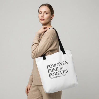 Model holding a white tote bag printed with “Forgiven Free Forever,” “Colossians 1:14,” and a small cross graphic.