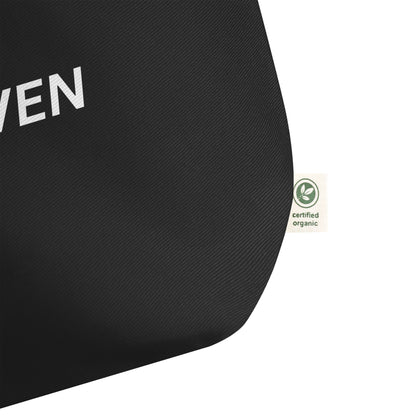 Close-up of the black cotton tote fabric, showing the textured weave and a side “certified organic” tag detail.