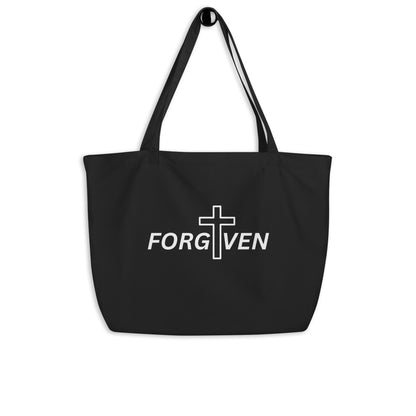 Large black cotton tote bag hanging on a hook featuring “FORGIVEN” with a white cross design on the front.