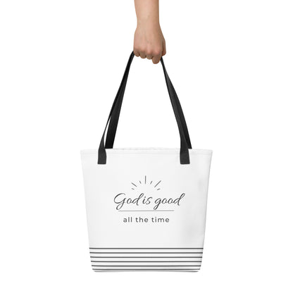 White tote bag held in hand featuring dark gray “God is good all the time” text with gray stripe accents near the base.