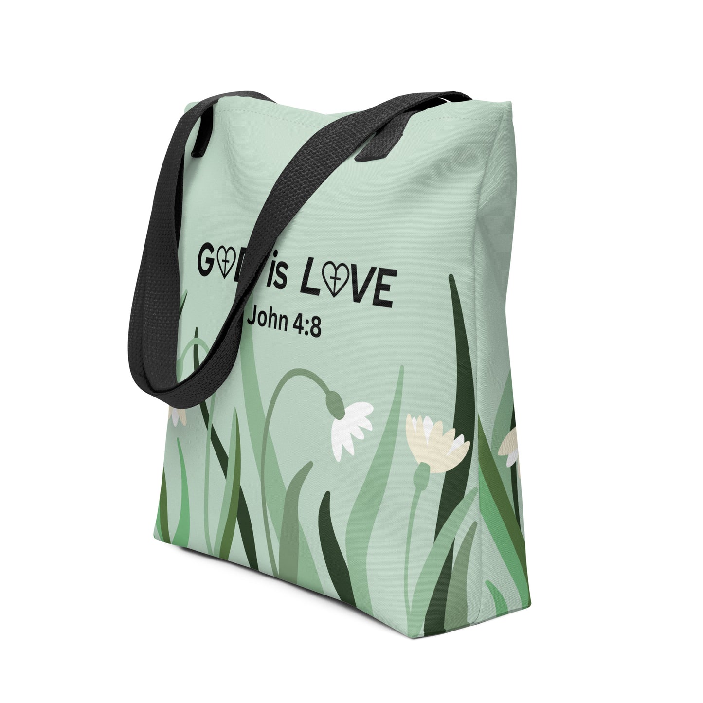 Angled view of sage green tote bag featuring “GOD is LOVE” and “1 John 4:8” over a floral-and-grass illustration, with black straps.