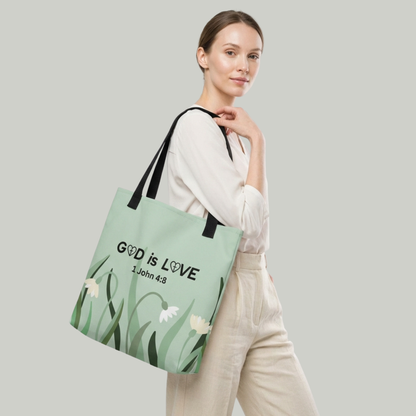 Lifestyle photo of a model carrying the sage green “GOD is LOVE” (1 John 4:8) Christian tote bag with floral design and black straps.