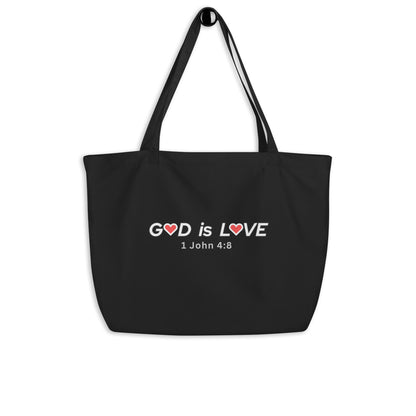 Large black cotton tote bag hanging on a hook featuring “GOD is LOVE” with red heart accents and “1 John 4:8” below.