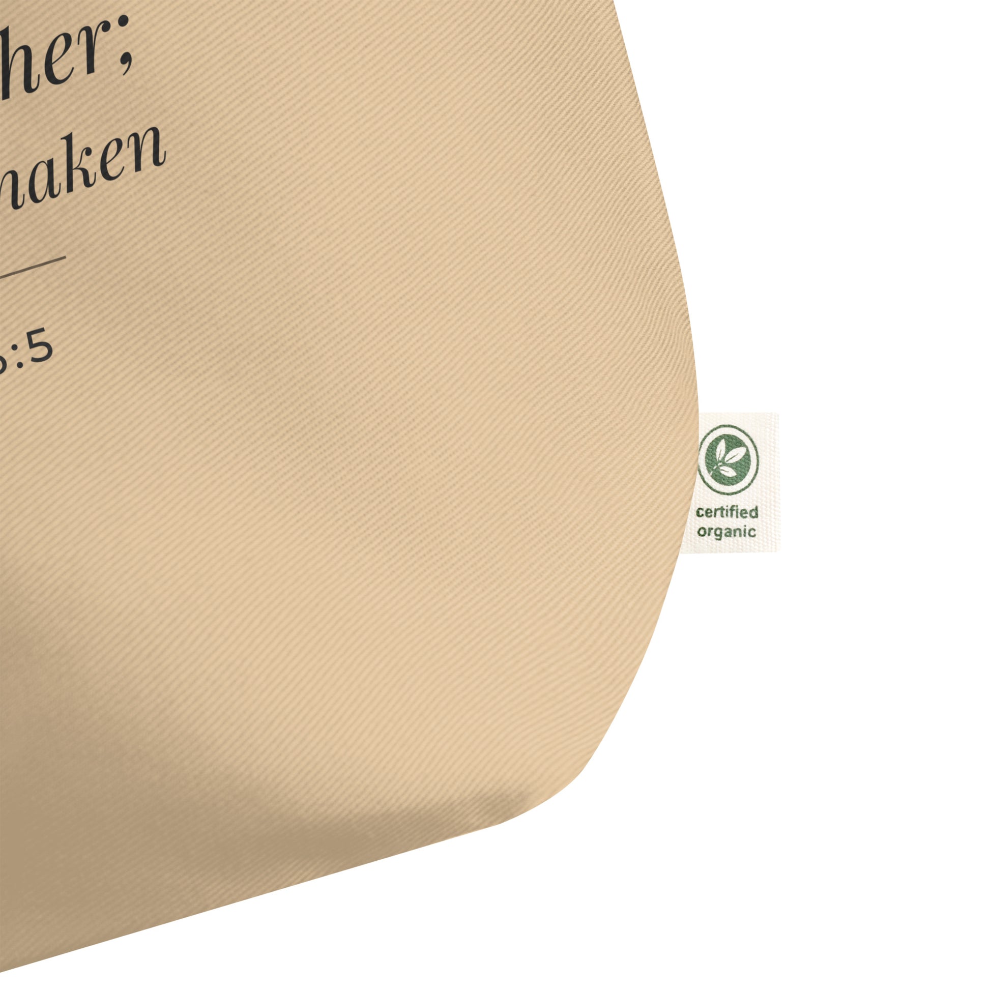 Close-up of a natural cotton Christian tote bag showing the beige fabric texture, certified organic side tag, and part of the Psalm 46:5 design.