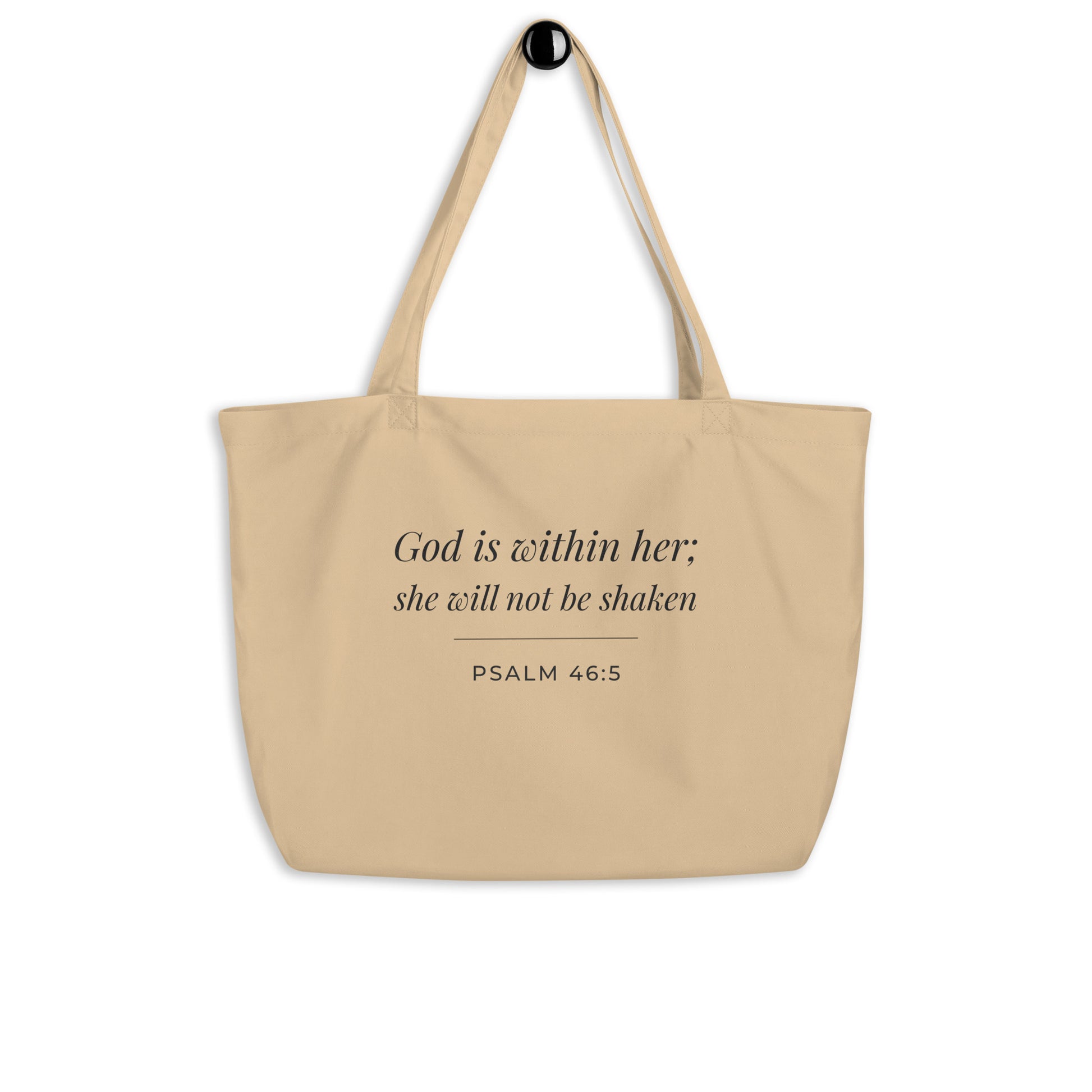 Natural cotton Christian tote bag hanging on a hook, featuring beige straps and a minimalist Psalm 46:5 faith design.