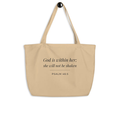 Natural cotton Christian tote bag hanging on a hook, featuring beige straps and a minimalist Psalm 46:5 faith design.