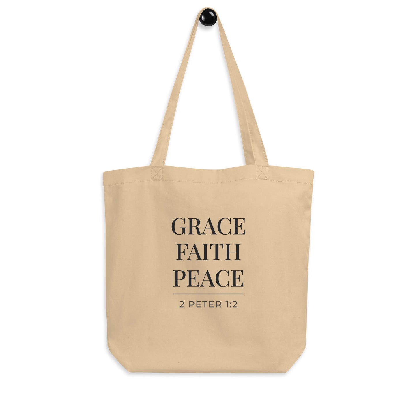 Cotton tote bag hanging on a hook with the words “Grace Faith Peace” and the scripture reference “2 Peter 1:2.”