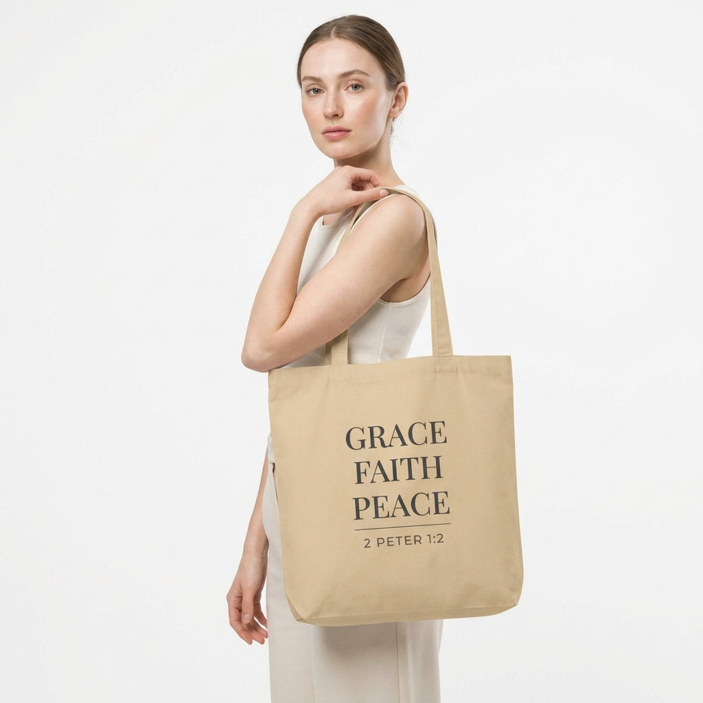 Model holding a natural cotton tote bag printed with “Grace Faith Peace” and “2 Peter 1:2.”