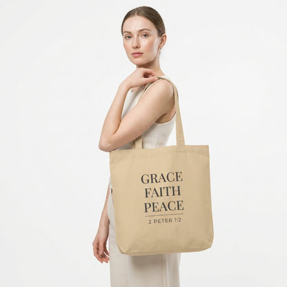 Model holding a natural cotton tote bag printed with “Grace Faith Peace” and “2 Peter 1:2.”