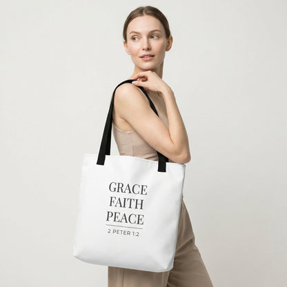 Model holding a white tote bag that reads “Grace Faith Peace” in dark gray with “2 Peter 1:2.”