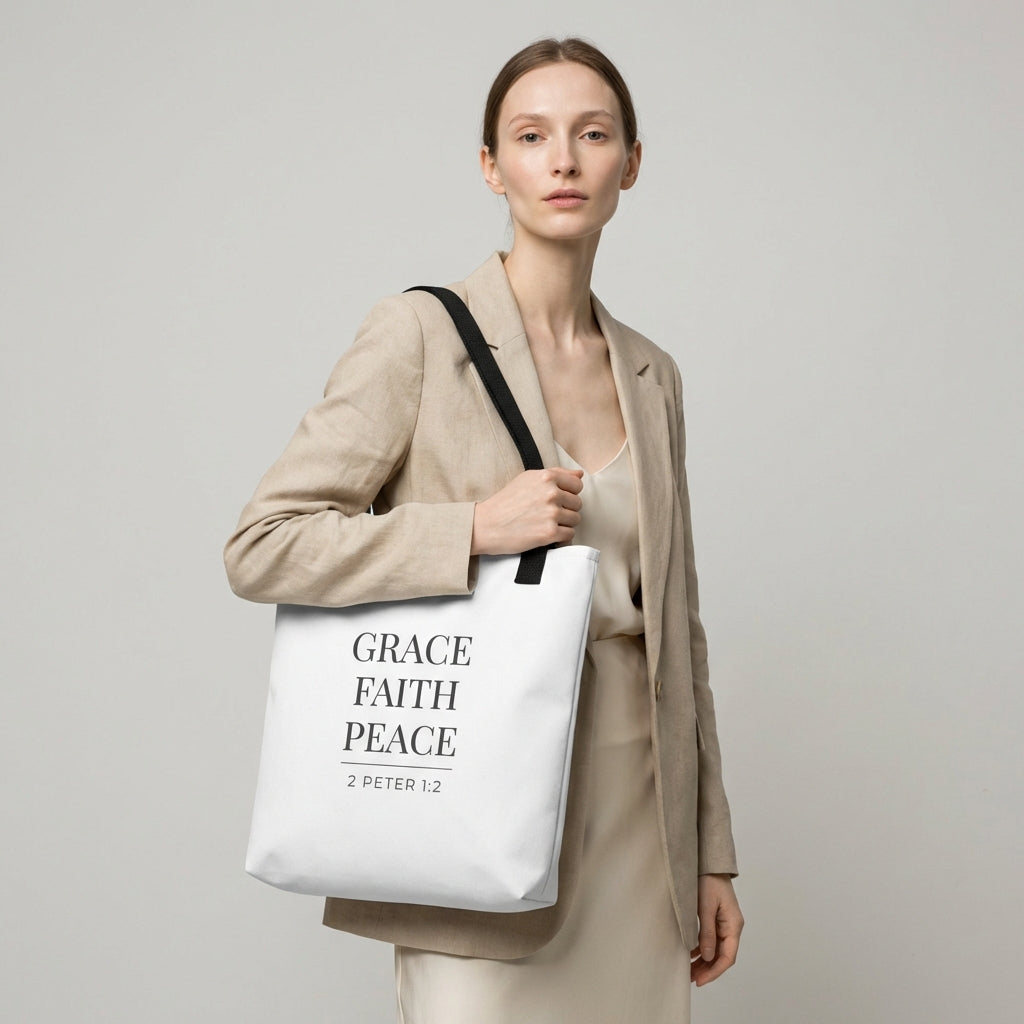 Model holding a white tote bag that reads “Grace Faith Peace” in dark gray with “2 Peter 1:2.”