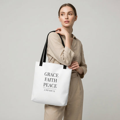 Model holding a white tote bag that reads “Grace Faith Peace” in dark gray with “2 Peter 1:2.”