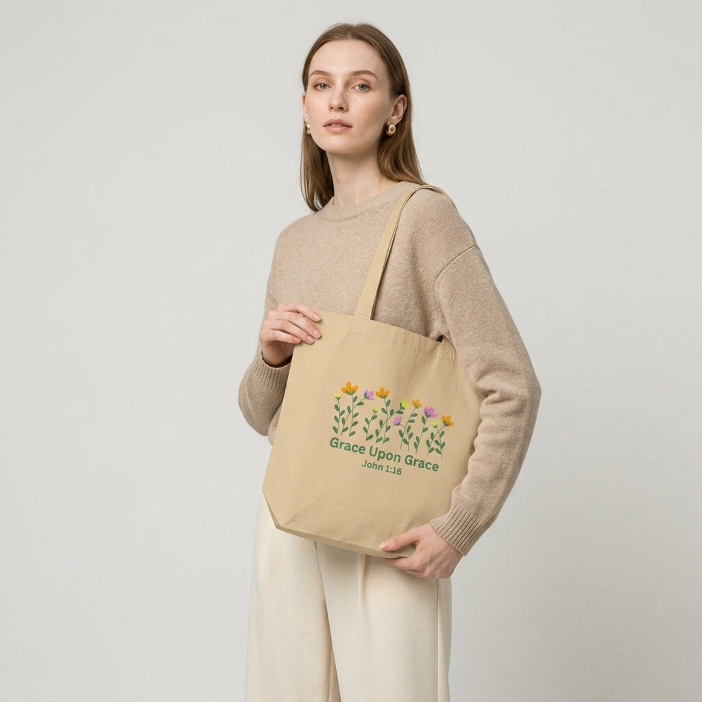 Model carrying a beige cotton tote bag with floral artwork and the text “Grace Upon Grace” and “John 1:16.”