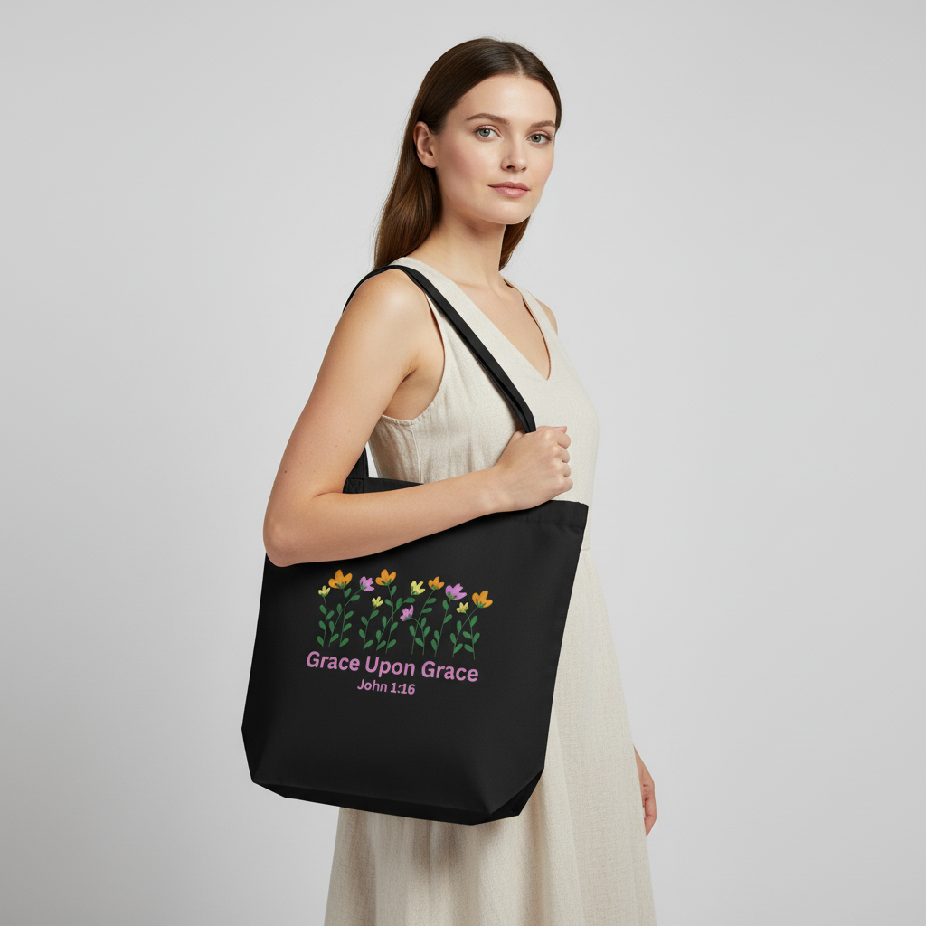 Model holding a black cotton tote bag with a floral graphic and pink “Grace Upon Grace” John 1:16 text on the front.