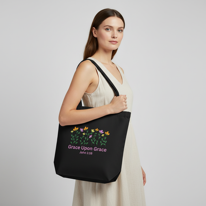 Model holding a black cotton tote bag with a floral graphic and pink “Grace Upon Grace” John 1:16 text on the front.