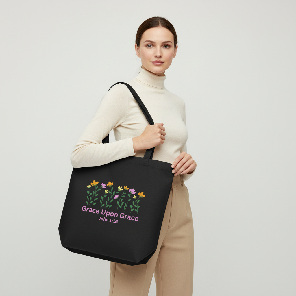 Model holding a black cotton tote bag with a floral graphic and pink “Grace Upon Grace” John 1:16 text on the front.