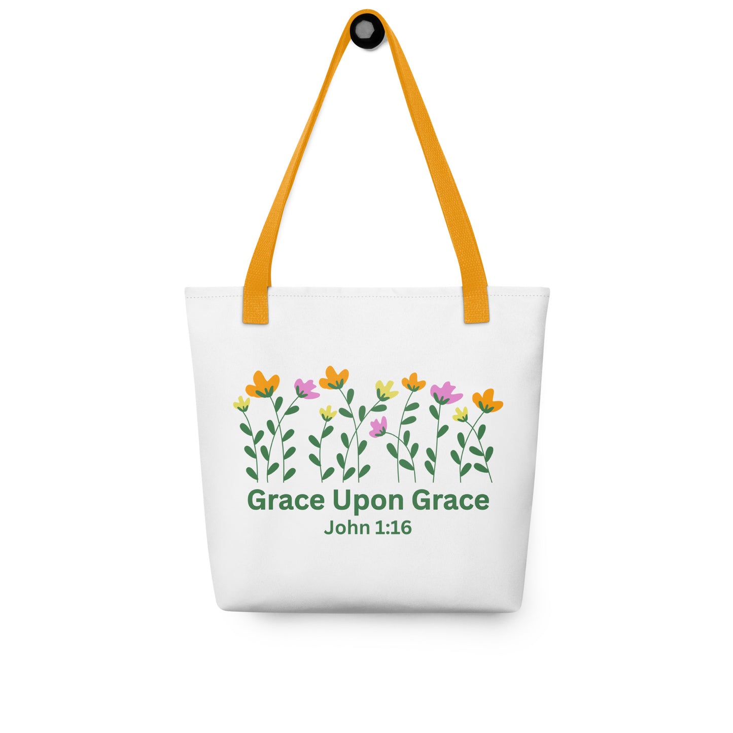 White ‘Grace Upon Grace’ John 1:16 tote bag hanging on a hook, featuring mustard-yellow straps and a floral design above green lettering.