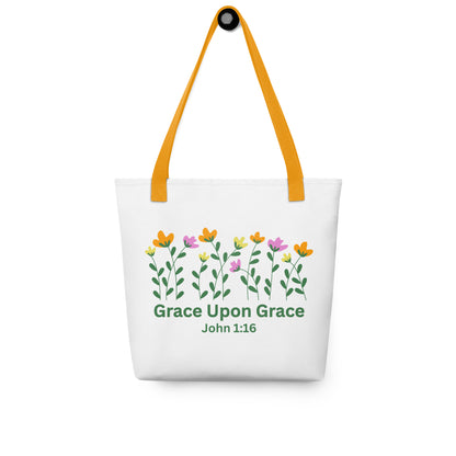 White ‘Grace Upon Grace’ John 1:16 tote bag hanging on a hook, featuring mustard-yellow straps and a floral design above green lettering.