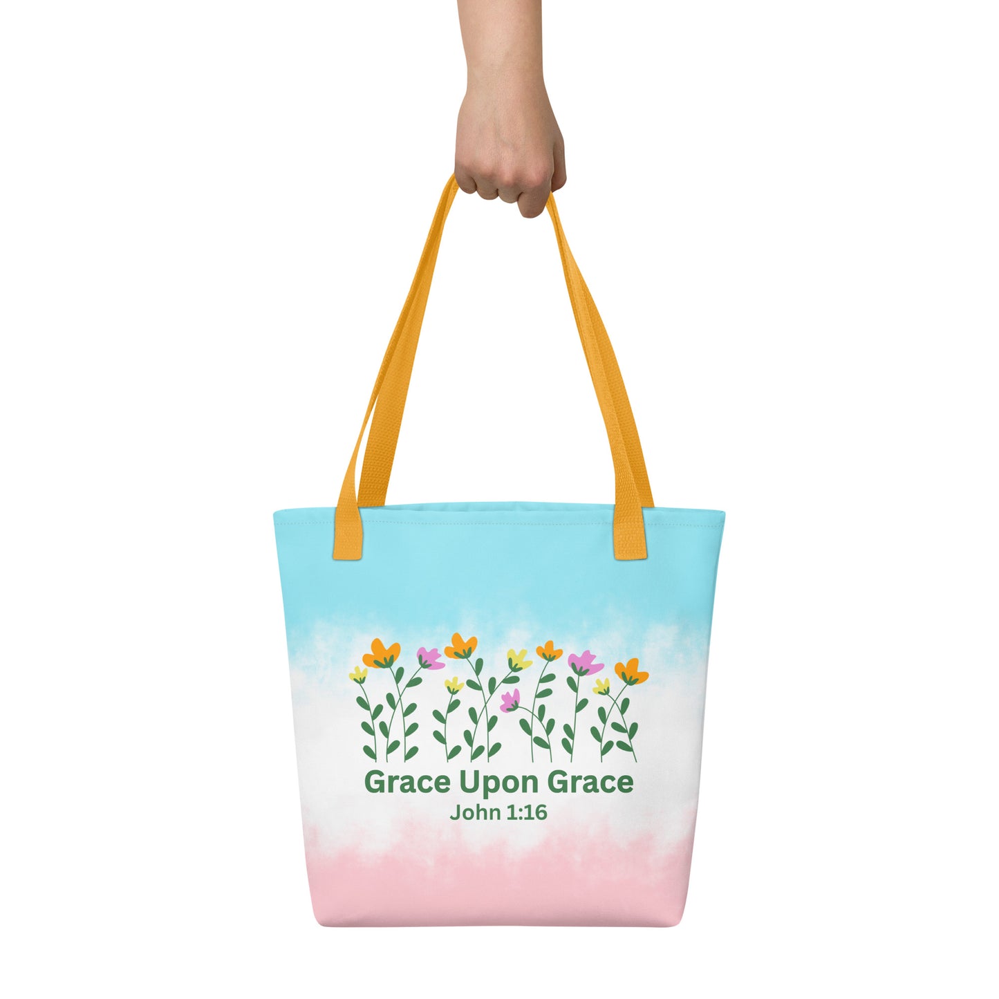 Person holding a pastel Christian tote bag with yellow handles, floral artwork, and the inspirational Bible verse design “Grace Upon Grace John 1:16.”