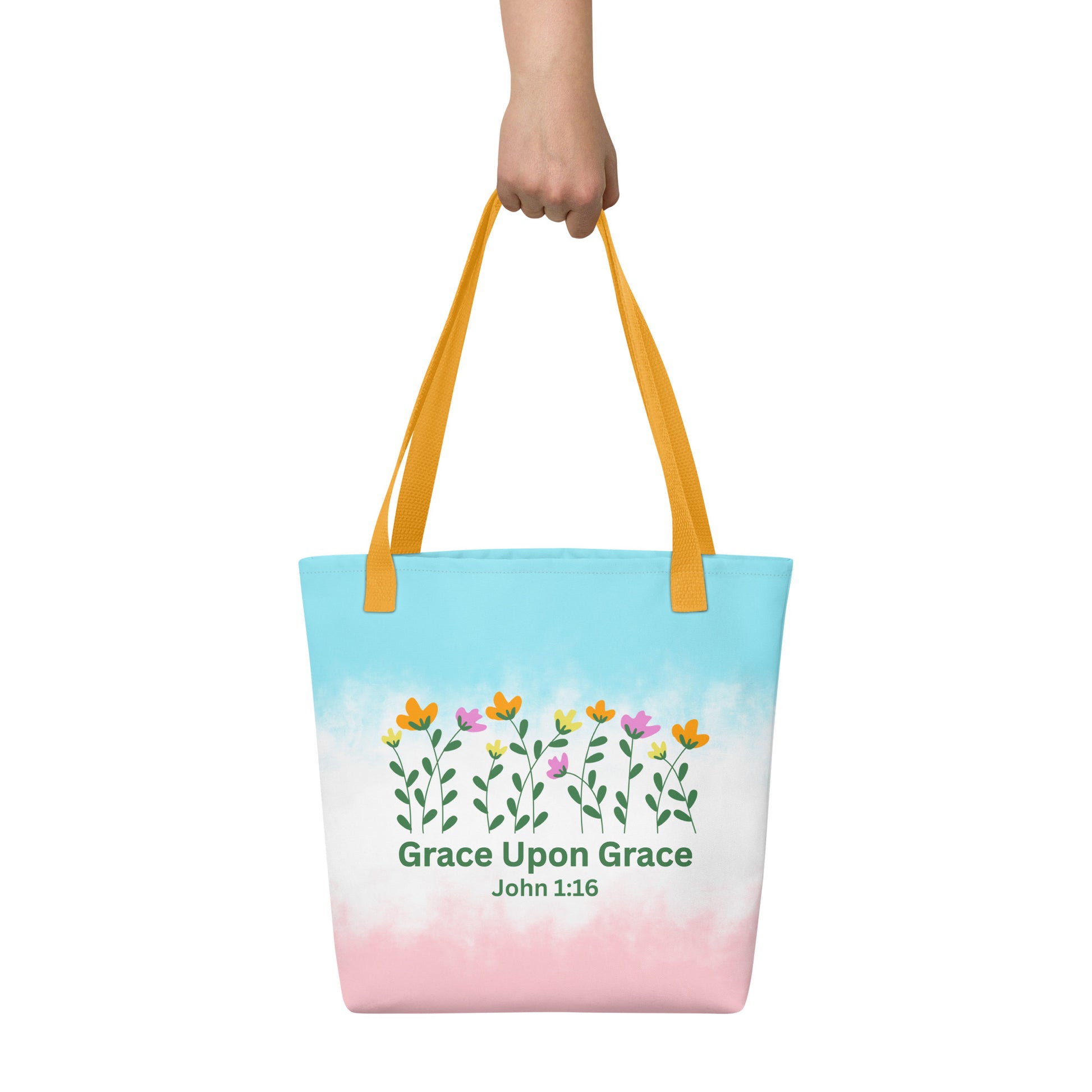 Person holding a pastel Christian tote bag with yellow handles, floral artwork, and the inspirational Bible verse design “Grace Upon Grace John 1:16.”