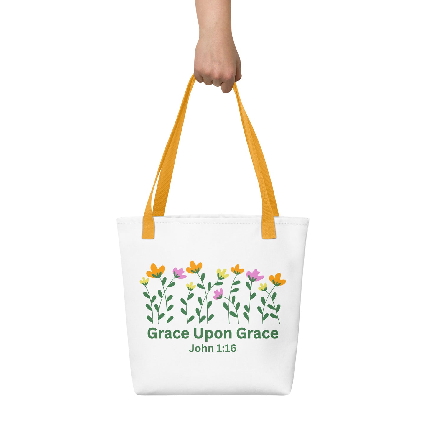 A hand holding the white ‘Grace Upon Grace’ John 1:16 tote bag with mustard-yellow straps; floral graphic and green text visible.